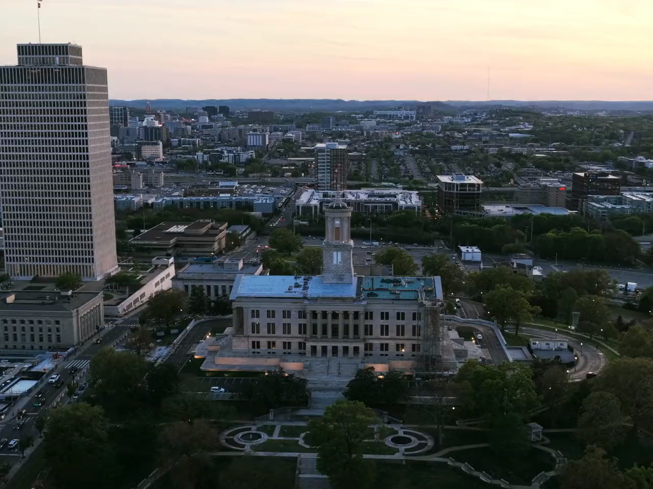 Golden hour aerial of a civic quarter, a stone administration building among office towers